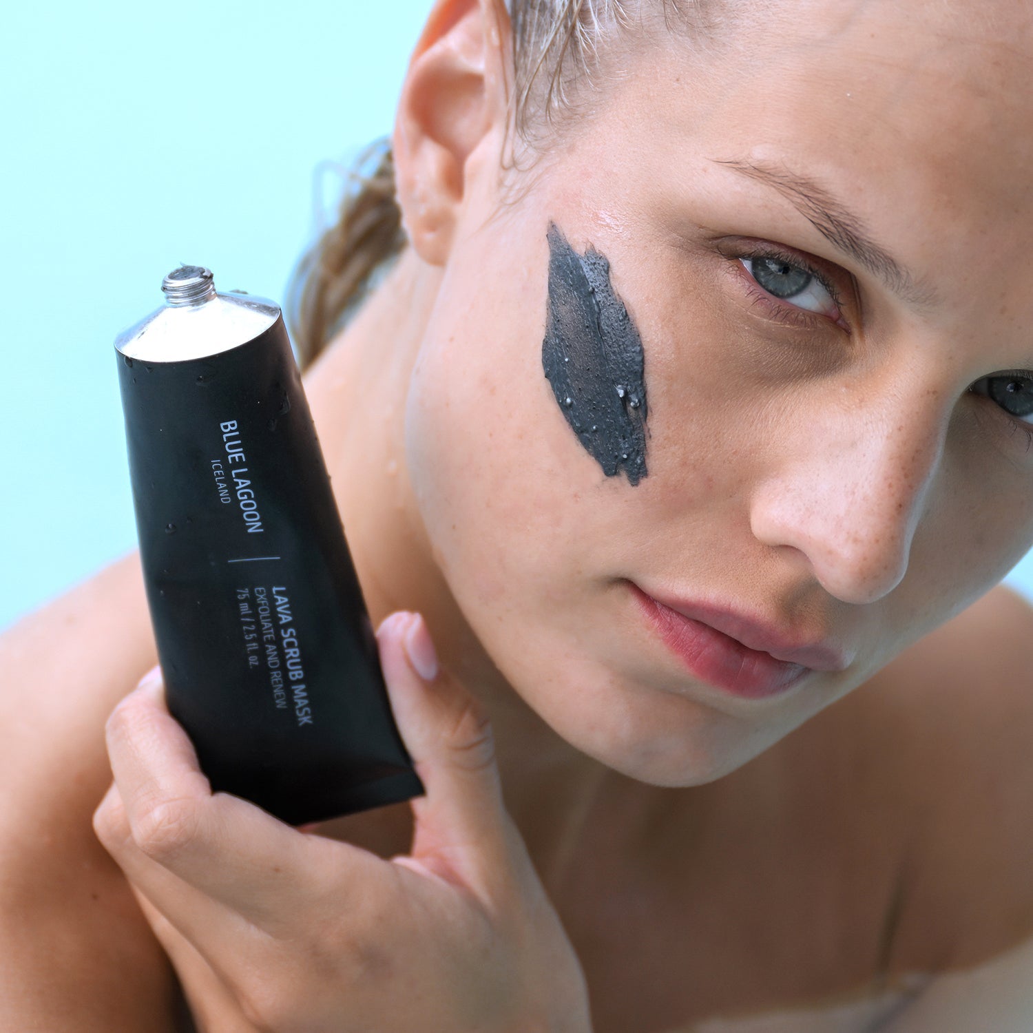 Model with Lava Scrub Mask applied to cheek holding tube