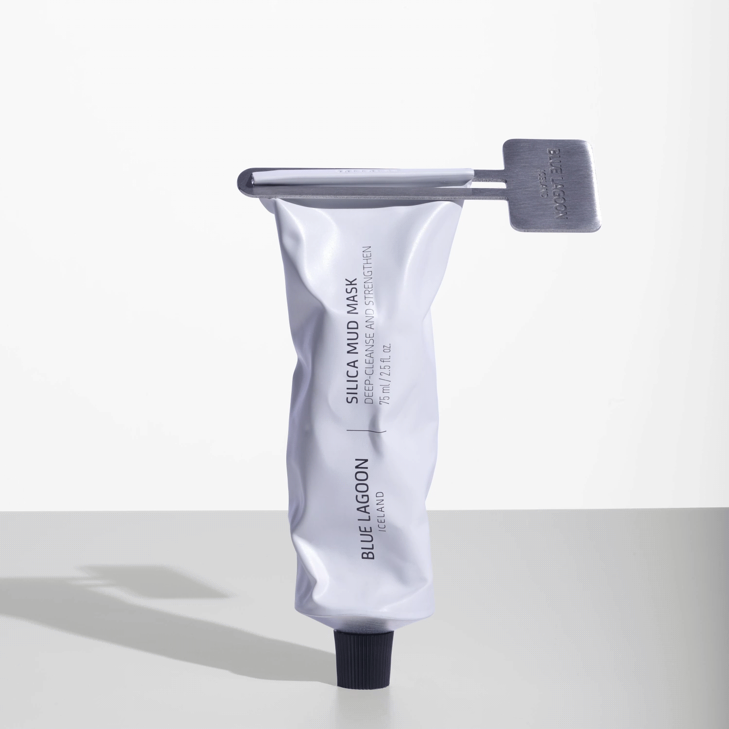 Tube/Mask Squeezer Key attached to aluminum skincare tube on white surface